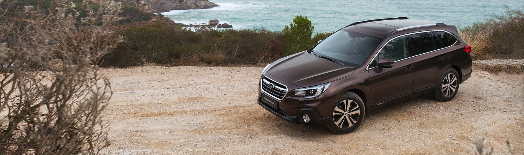 Subaru Outback parked by the sea on gravel